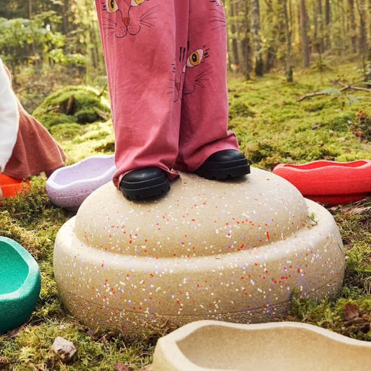 Kind steht draußen auf einem sandfarbenen, gesprenkelten Grow-Stein im Garten und balanciert