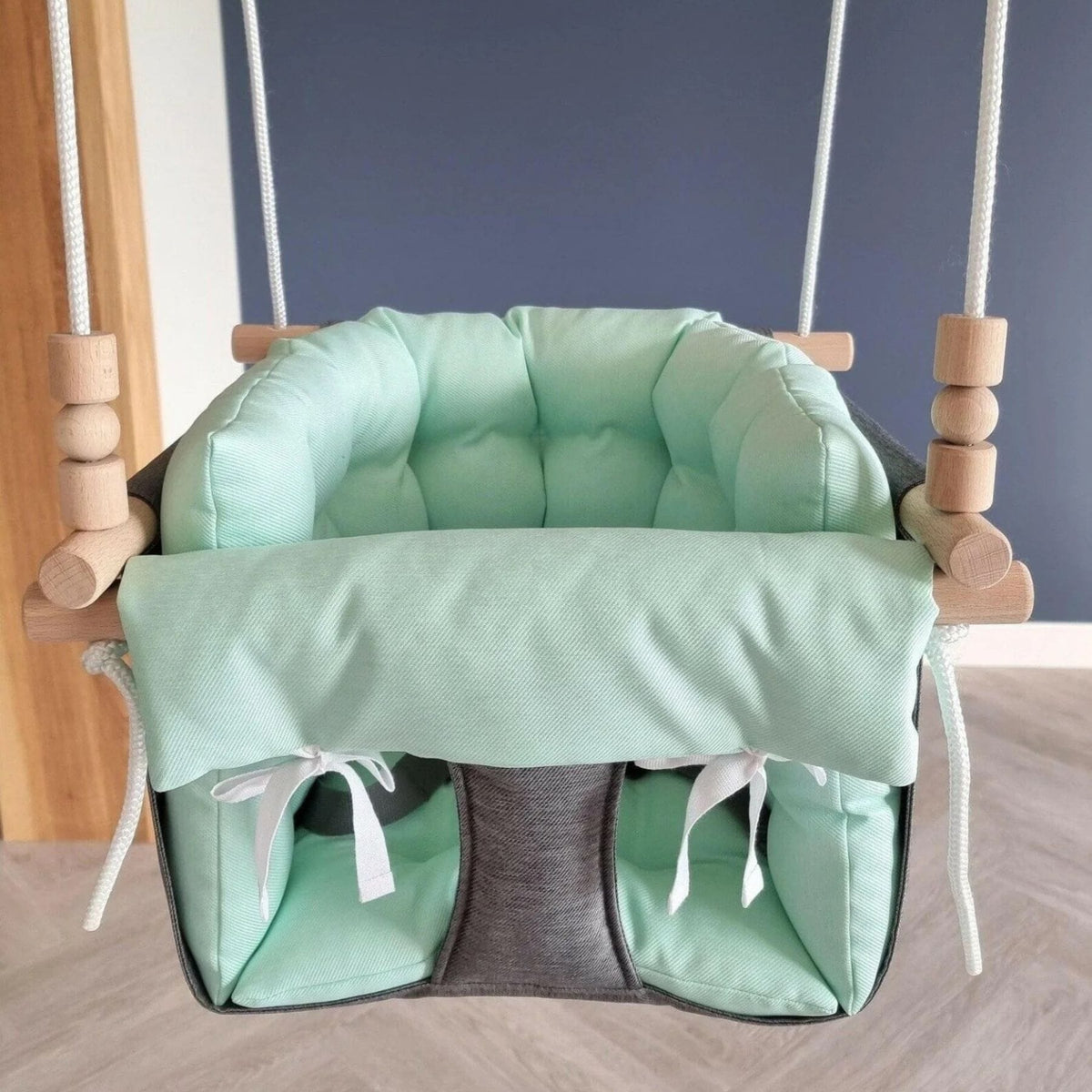 Schaukel mit mintfarbenen Kissen und dunkelgrauem Stoffsteg vor einer blauen Wand